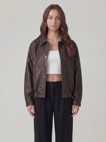 Woman wearing a brown jacket over a white top and black pants on a plain background