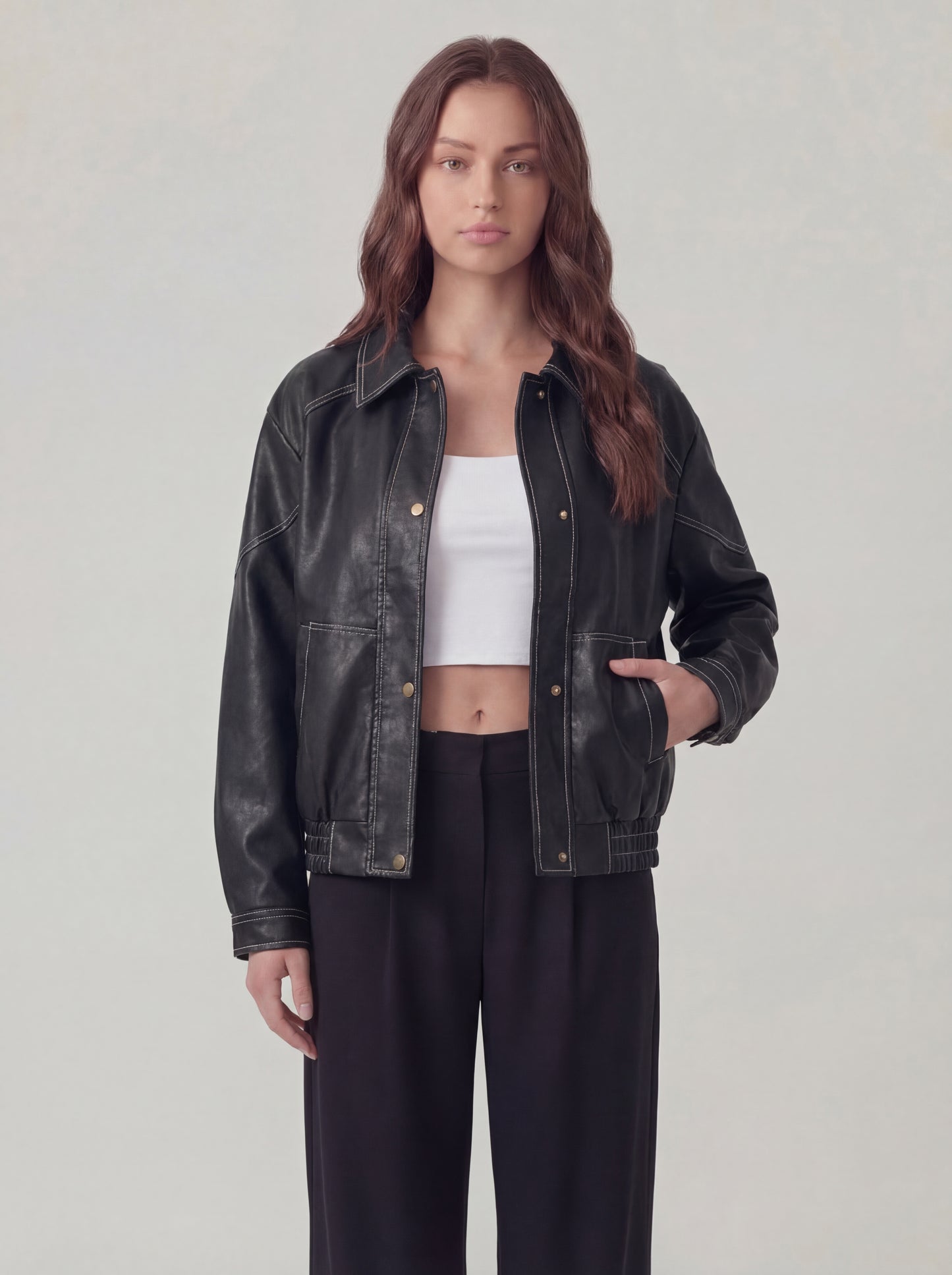 Woman wearing a black leather jacket over a white top and black pants on a light gray background
