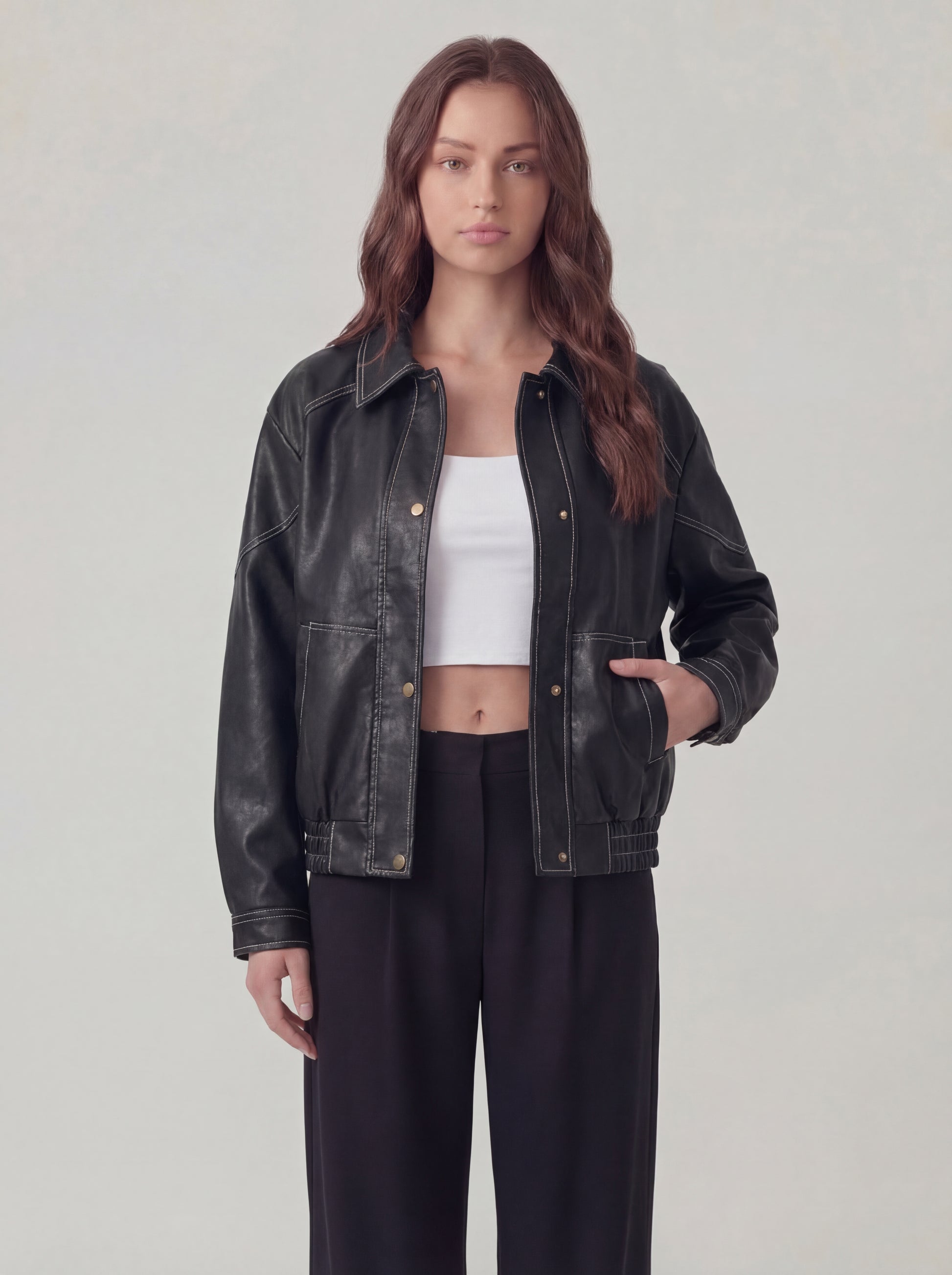 Woman wearing a black leather jacket over a white top and black pants on a light gray background