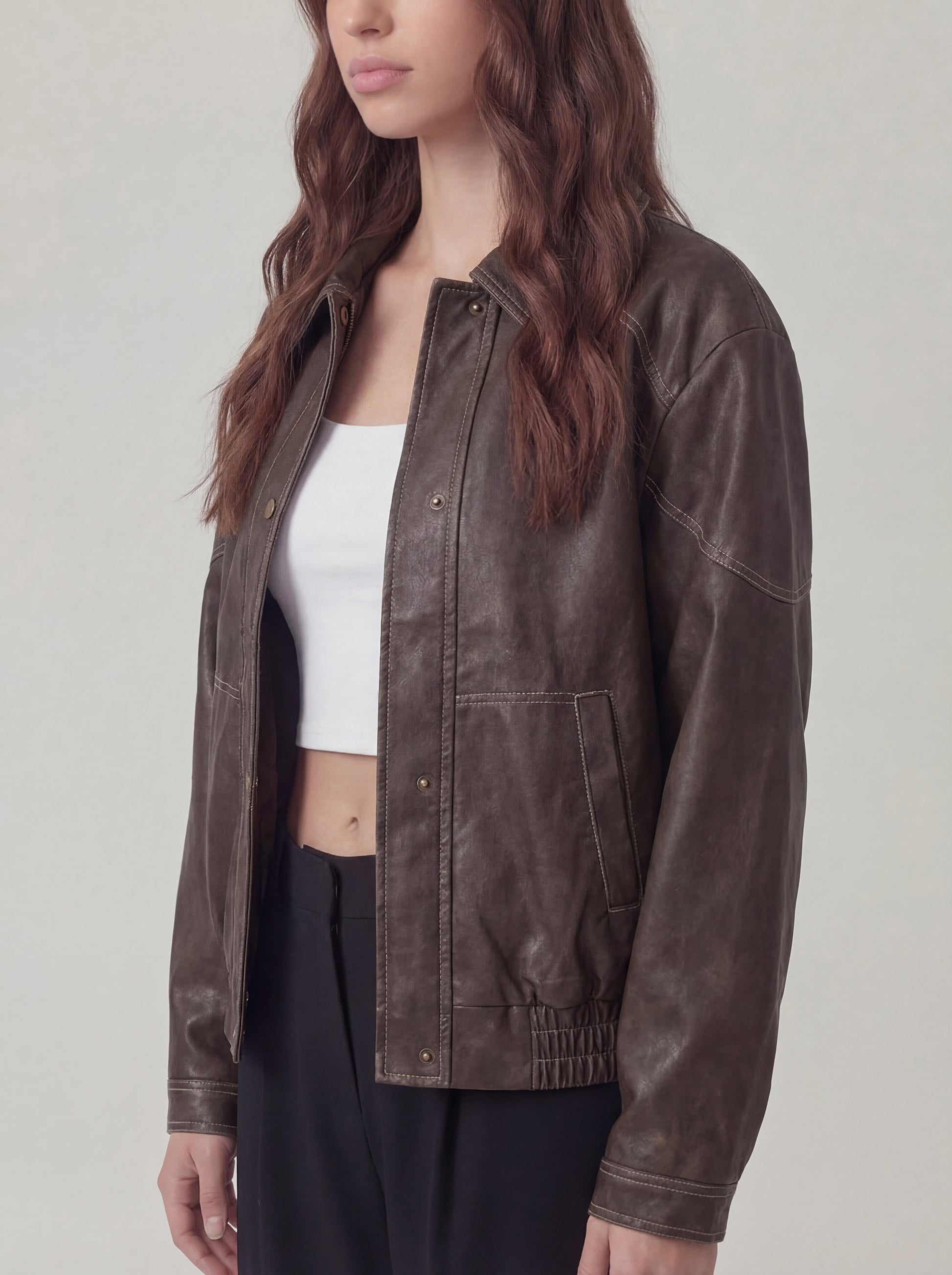 Person wearing a brown leather jacket over a white top and black pants on a plain background