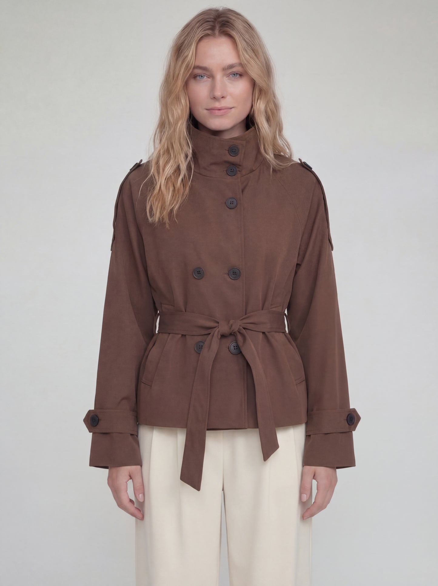 Woman wearing a brown coat with a belt on a plain background