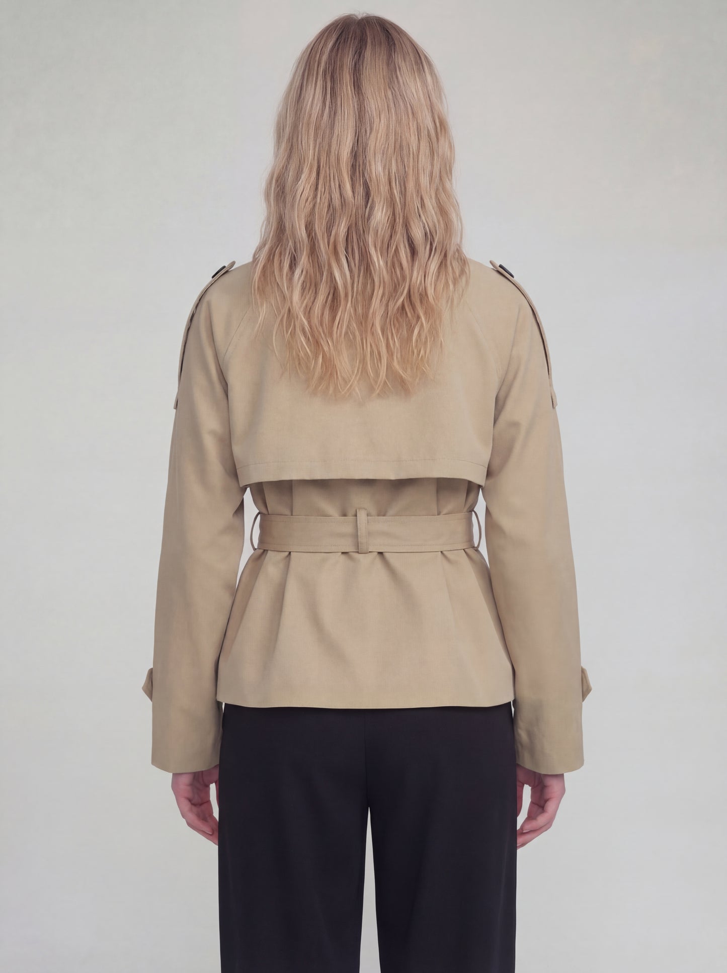 Person wearing a beige trench coat with a belt on a plain background