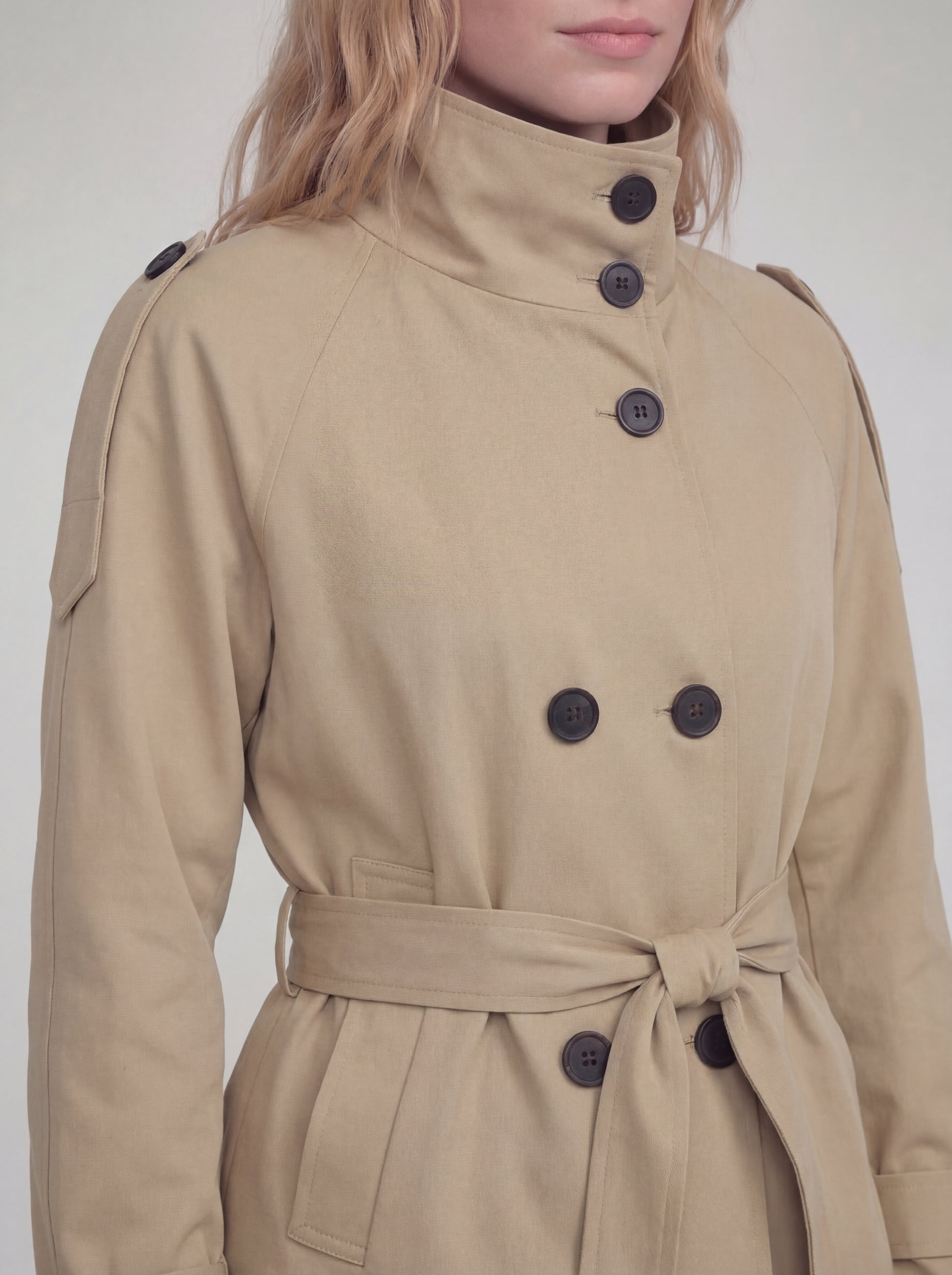 Beige trench coat with black buttons on a plain background