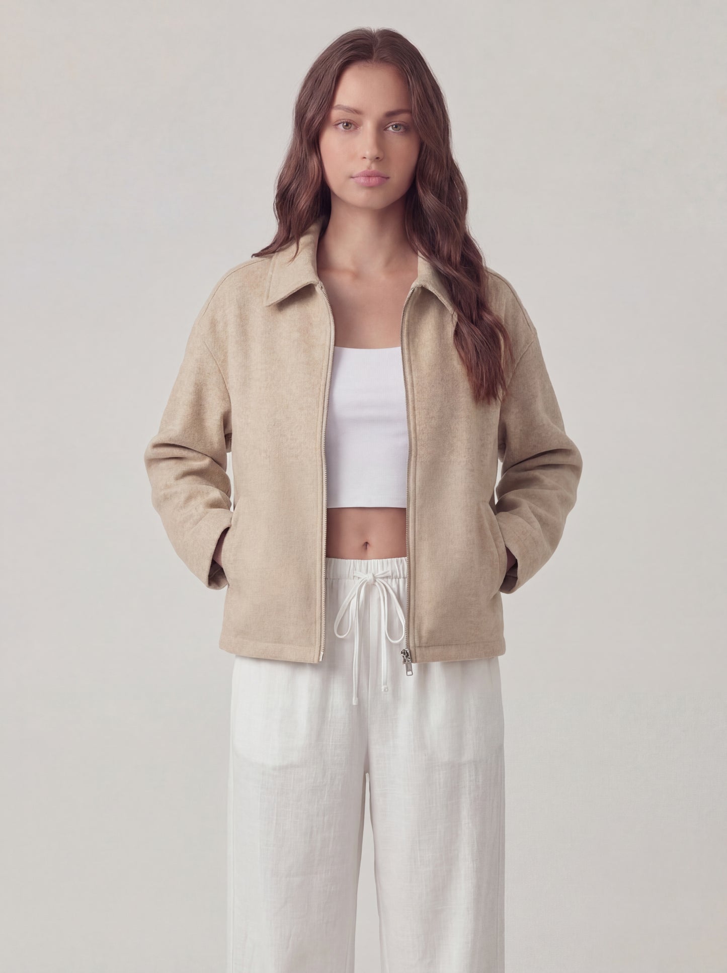 Woman wearing a beige jacket over a white top and pants on a plain background