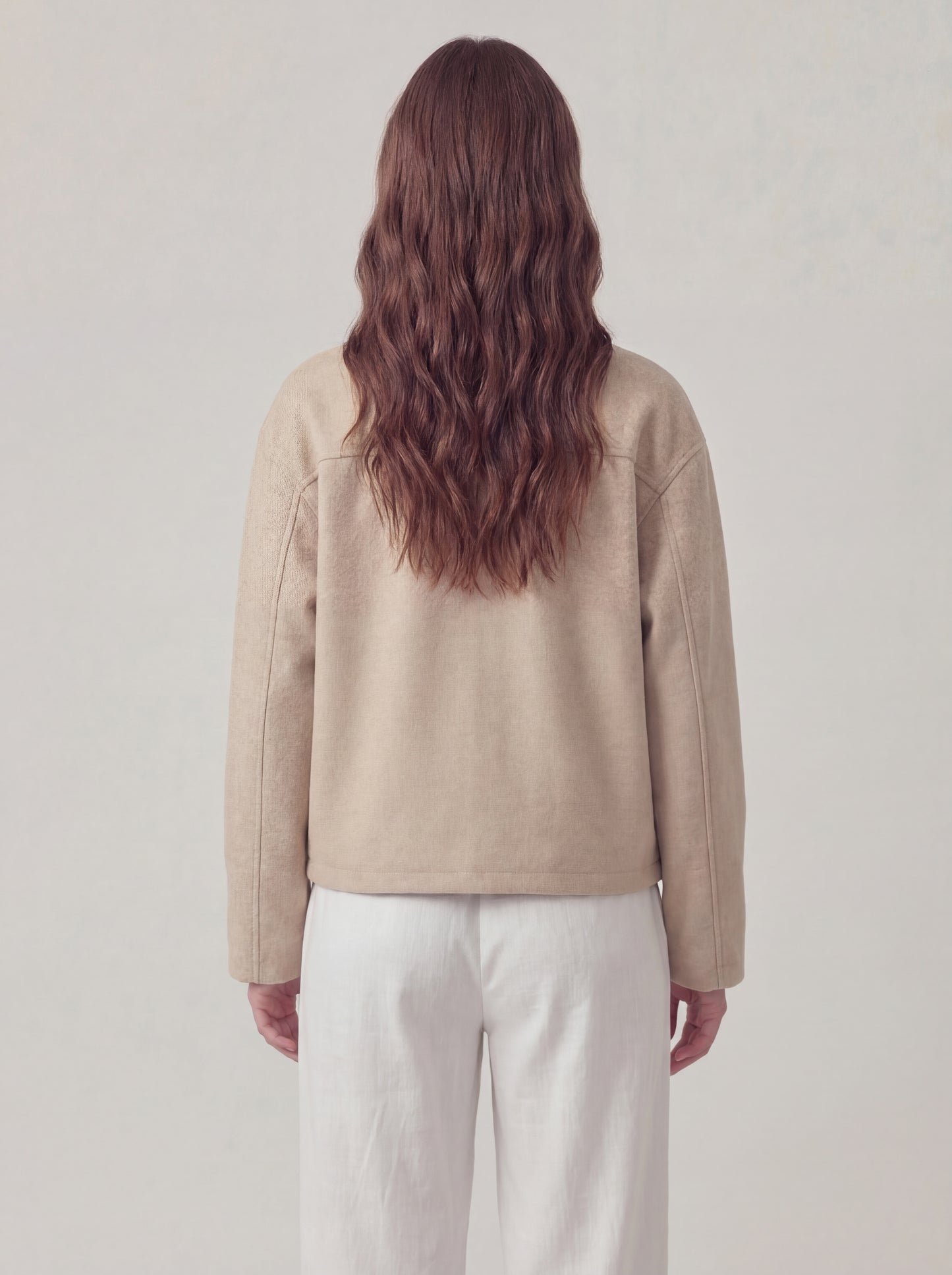 Person wearing a beige jacket and white pants against a plain background