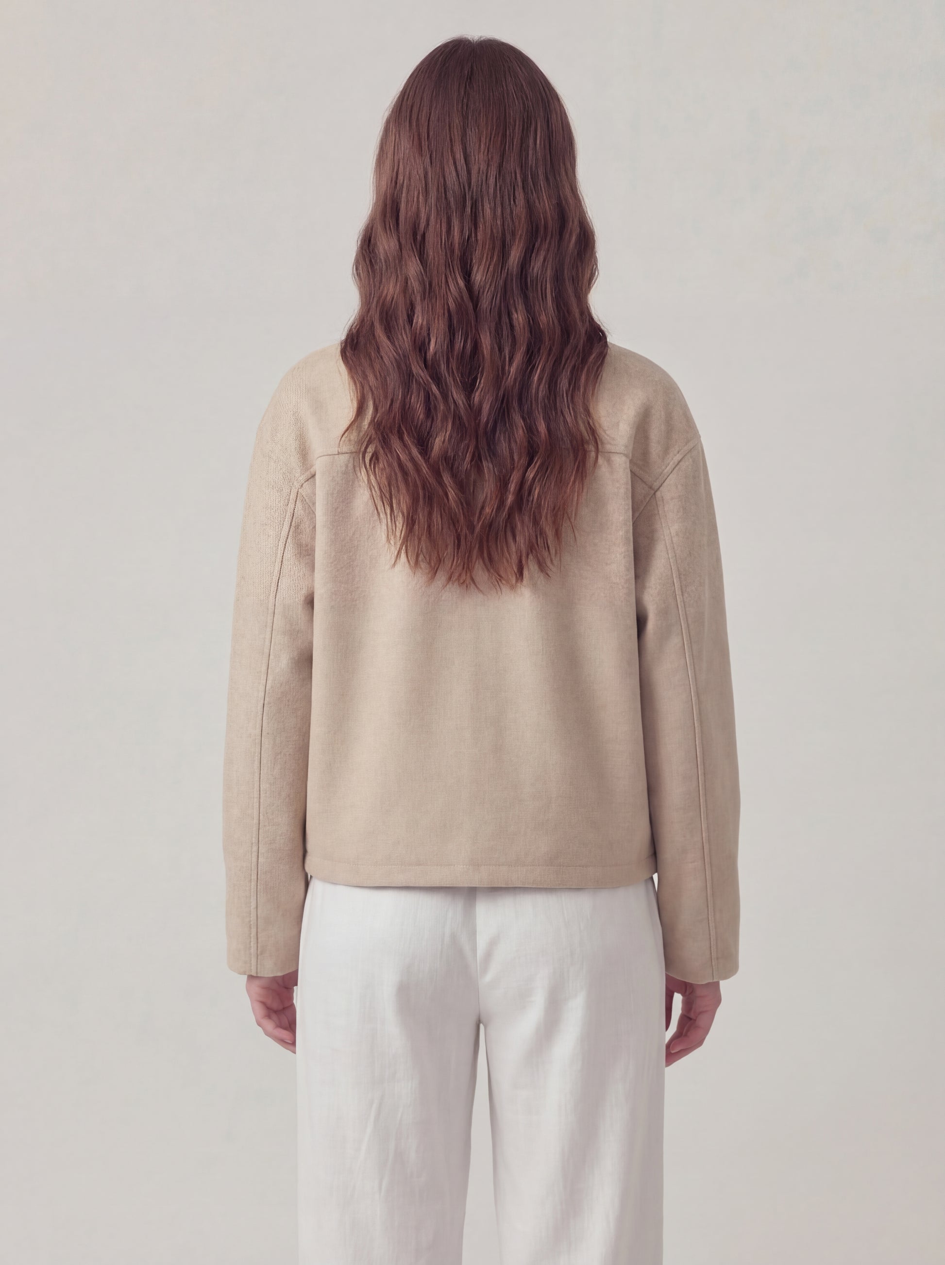Person wearing a beige jacket and white pants against a plain background