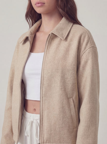Person wearing a beige jacket over a white top and pants on a light background