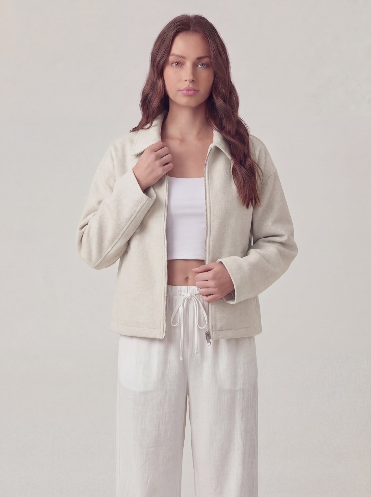 Woman wearing a beige jacket and white pants on a plain background