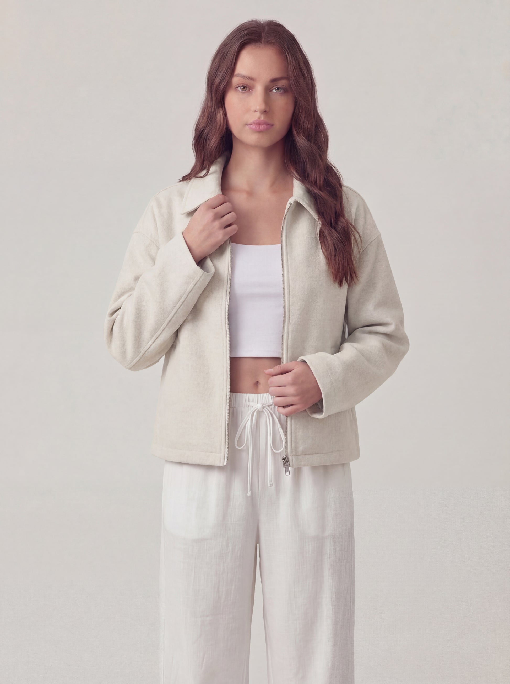 Woman wearing a beige jacket and white pants on a plain background