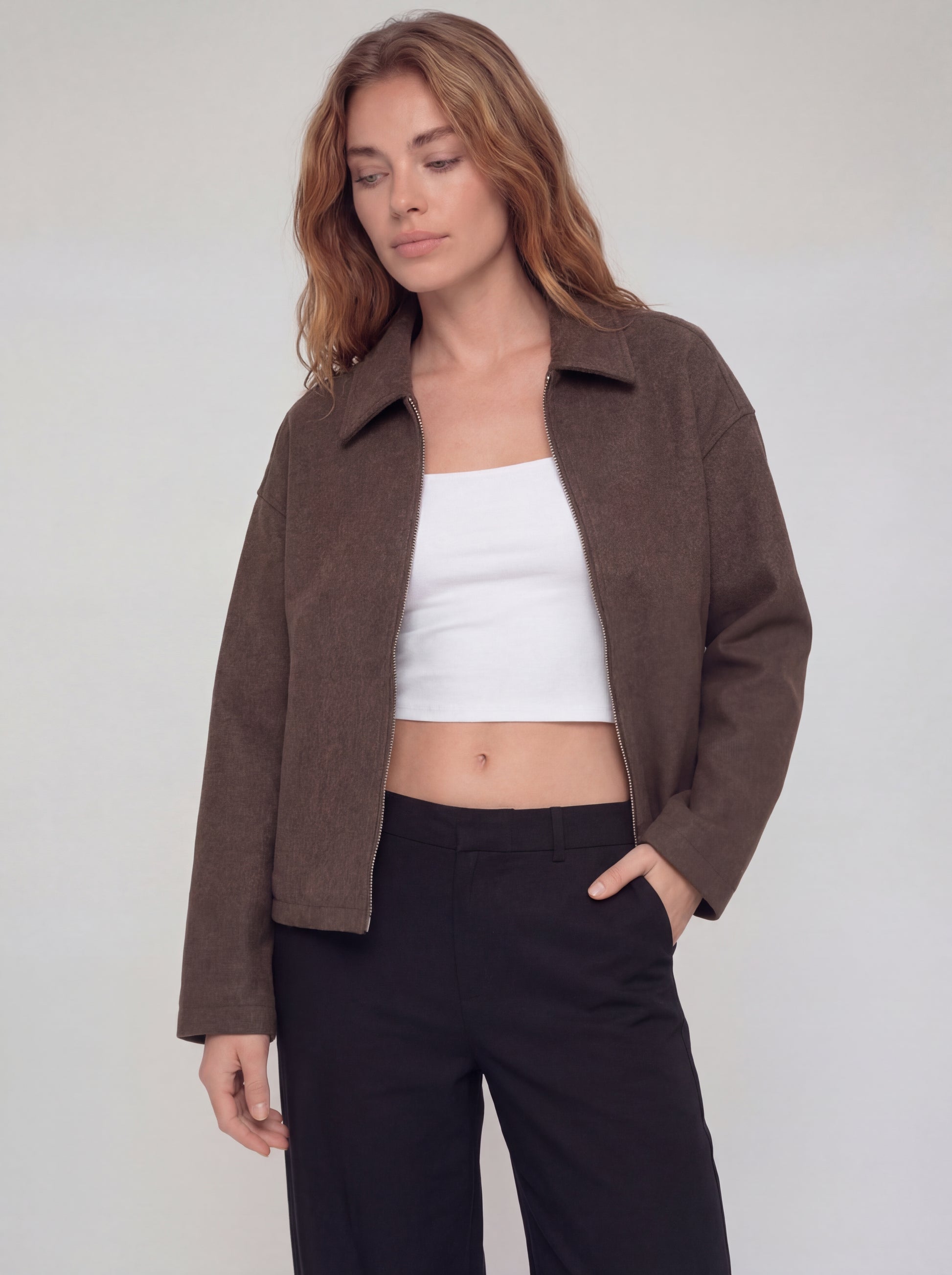 Woman wearing a brown jacket, white top, and black pants on a plain background