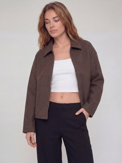 Woman wearing a brown jacket, white top, and black pants on a plain background