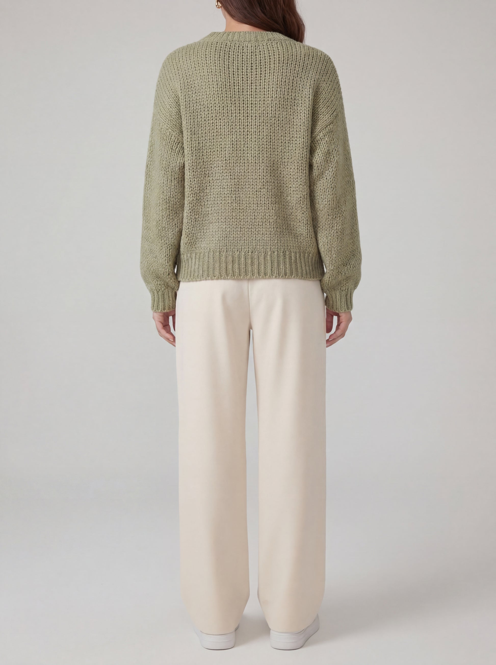 Person wearing a green knitted sweater and beige pants on a plain background