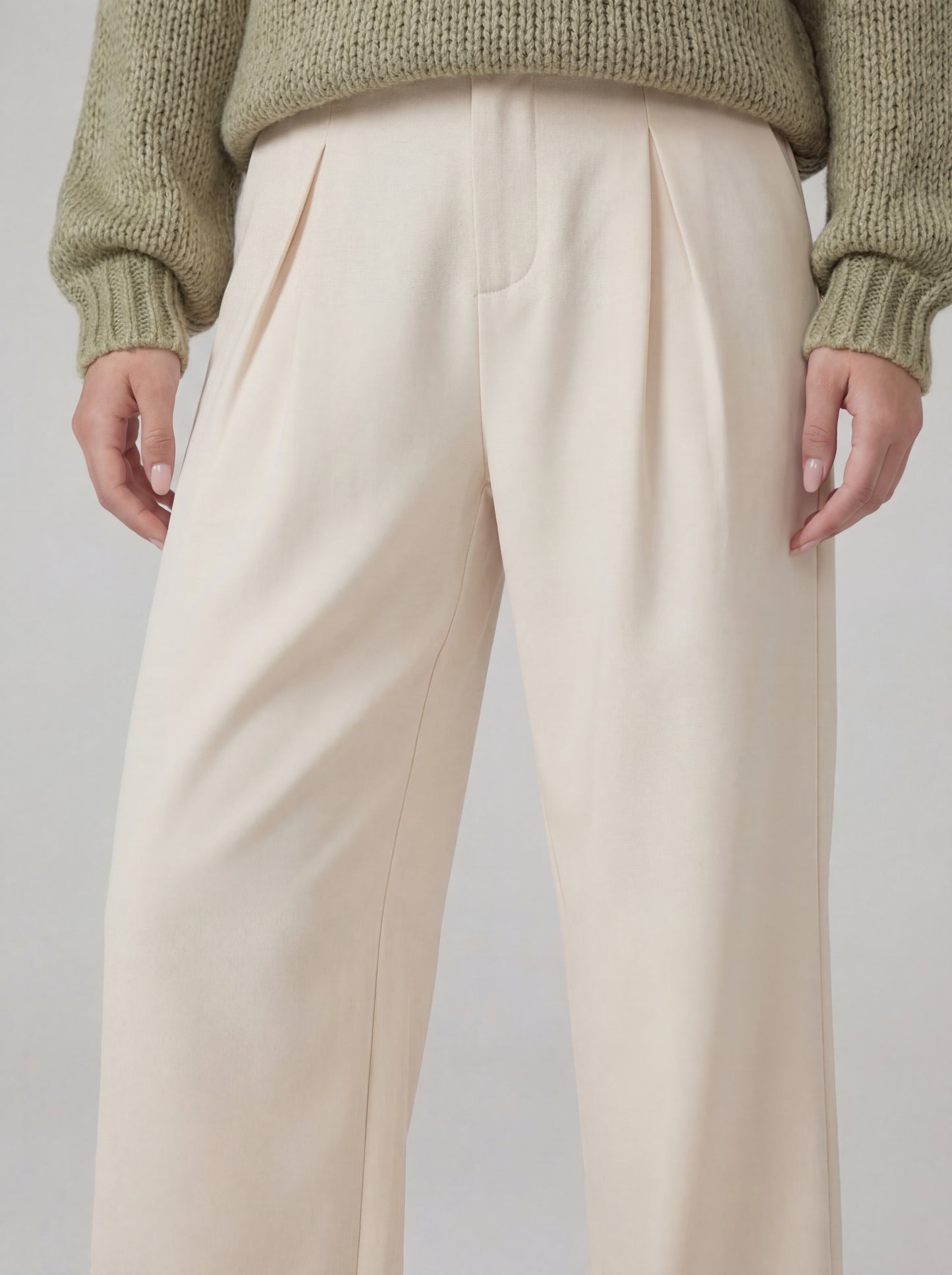 Beige pants worn with a green sweater on a plain background